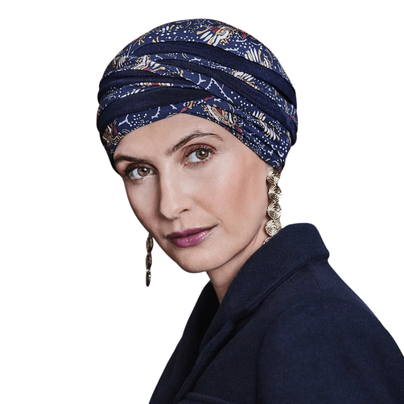 Turbante Shanti con estampado Amber Garden llevado por una mujer, mostrando el tocado azul oscuro con motivo de plumas y tallos