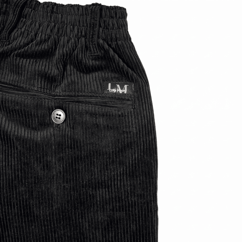 Primer plano de tela de pana negra, un bolsillo trasero con botón y la cintura elástica de los pantalones