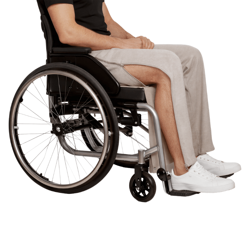 Una persona en silla de ruedas con pantalones de chándal grises y cremallera lateral abierta mostrando la pierna