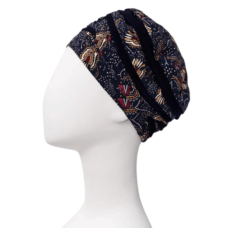 Turbante Shanti con estampado Amber Garden visto de lado en maniquí blanco, con base azul oscuro y motivo de plumas y tallos
