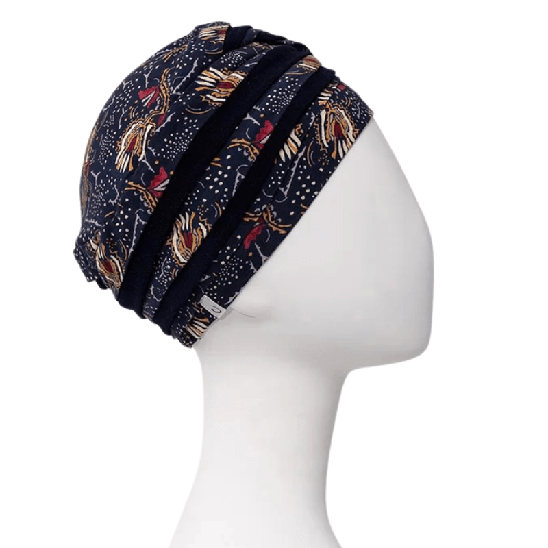 Turbante Shanti con estampado Amber Garden visto desde el lado derecho en maniquí, con colores azul oscuro y motivo de plumas y tallos