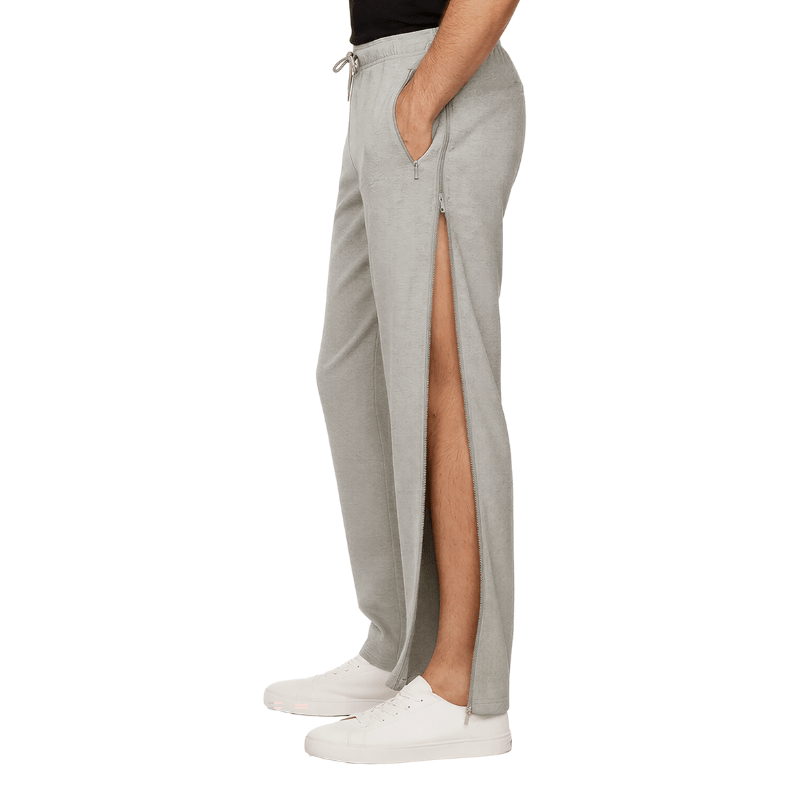 Pantalones de chándal grises con cremallera lateral abierta mostrando la pierna, vistos de lado en una persona