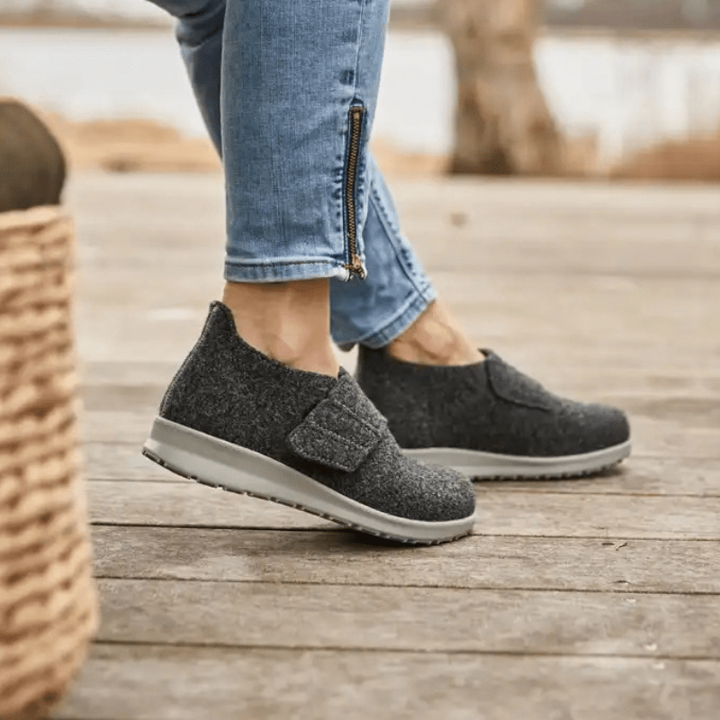Mujer con zapatillas New Feet gris antracita en un suelo de madera, vista lateral de los pies
