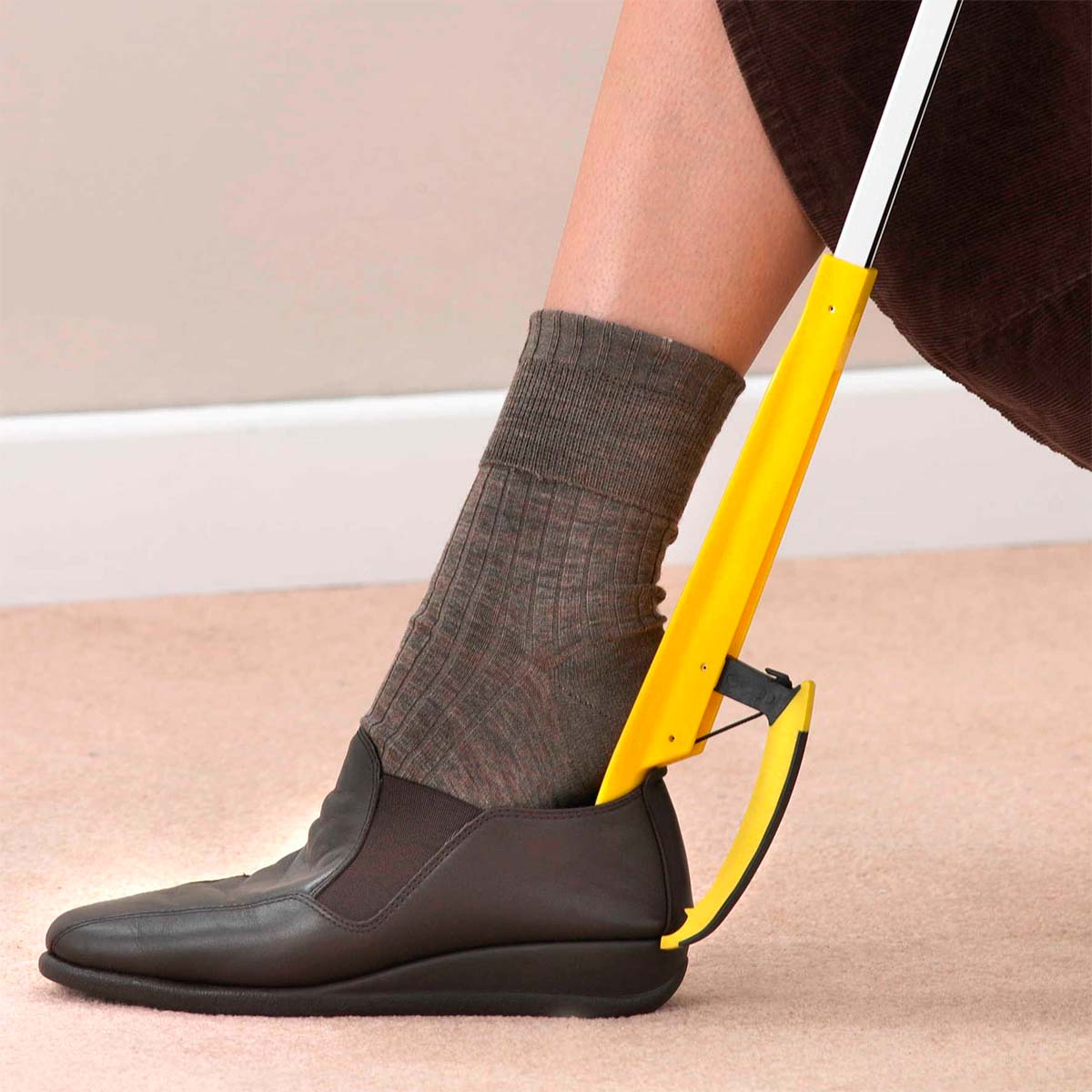 Una persona usa la pinza de agarre amarilla como calzador para ponerse un zapato marrón oscuro